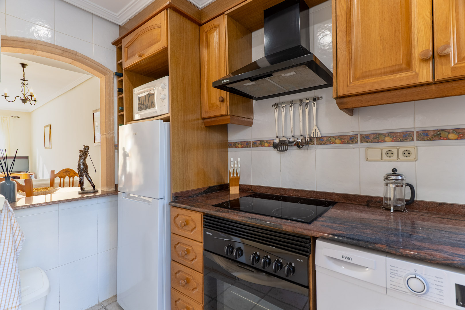 Functionele keuken met houten kasten, granieten werkblad en een decoratieve boog die uitkijkt op de aangrenzende woonruimte.