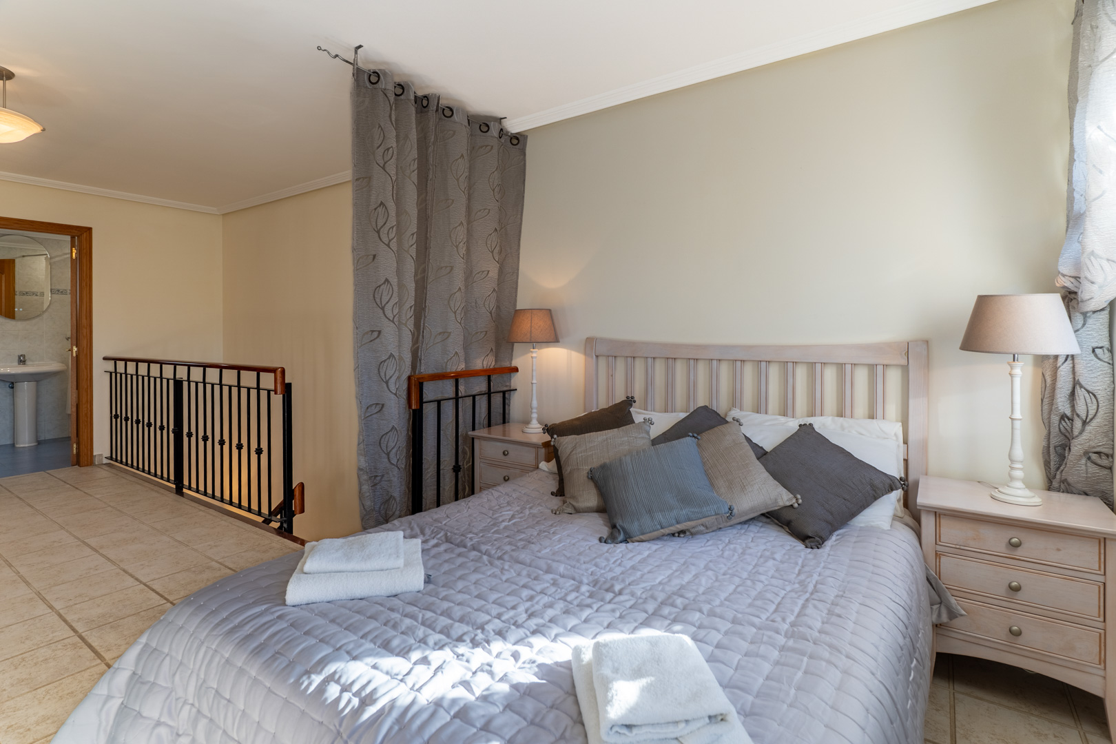 Hoofdslaapkamer op de bovenste verdieping met en-suite badkamer, keramische tegelvloer en een metalen balustrade bij de trap.