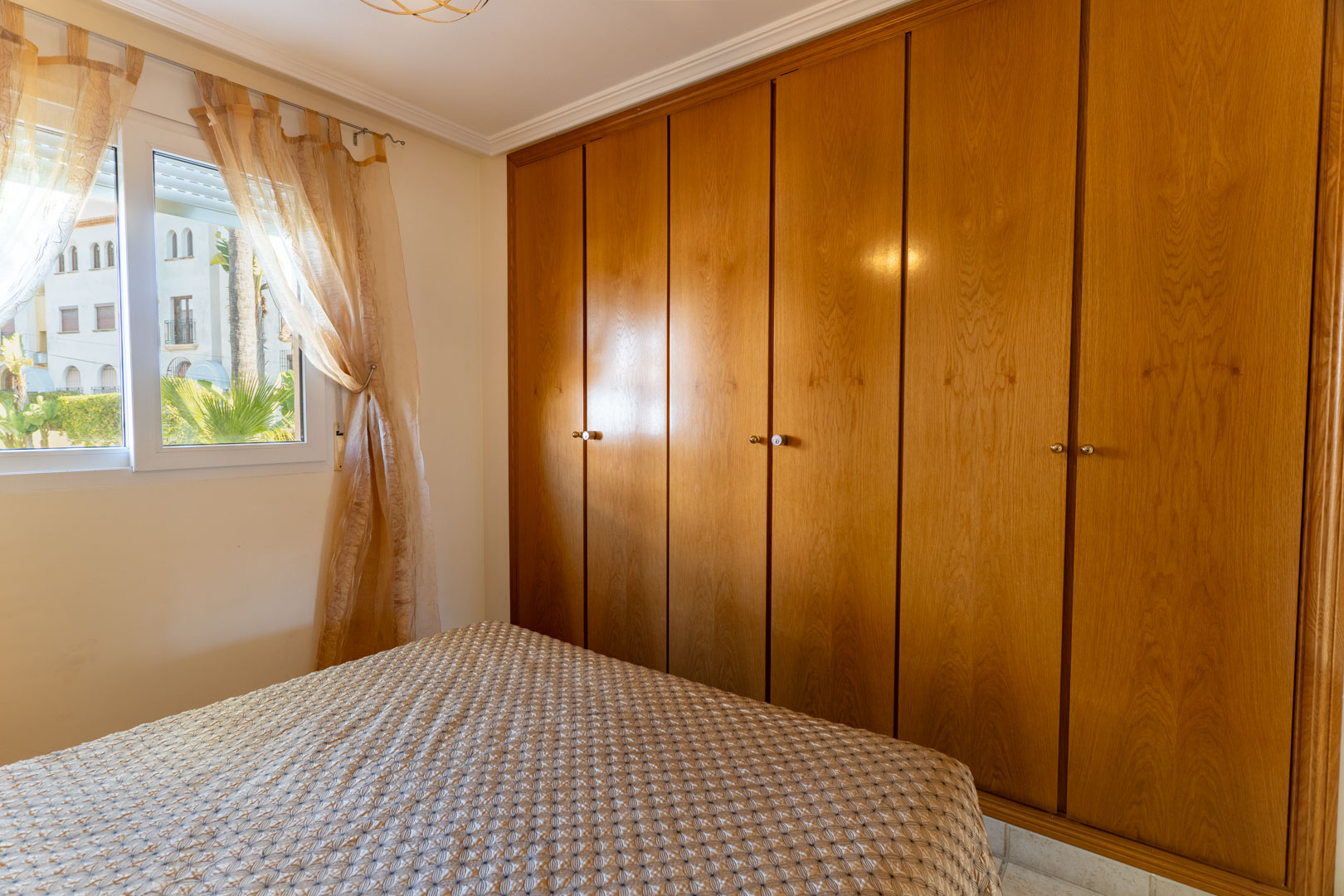 Slaapkamer met een grote zesdeurs ingebouwde houten kledingkast en een raam met uitzicht op de omliggende tuinen en natuurlijke lichtinval.