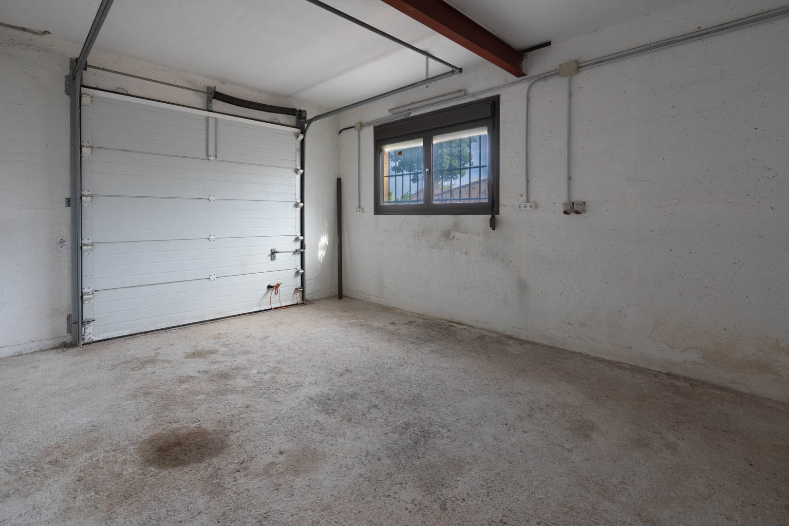 Functionele garage met betonnen vloer, witte sectionaaldeur en een raam met beveiligingsstangen voor natuurlijk daglicht.