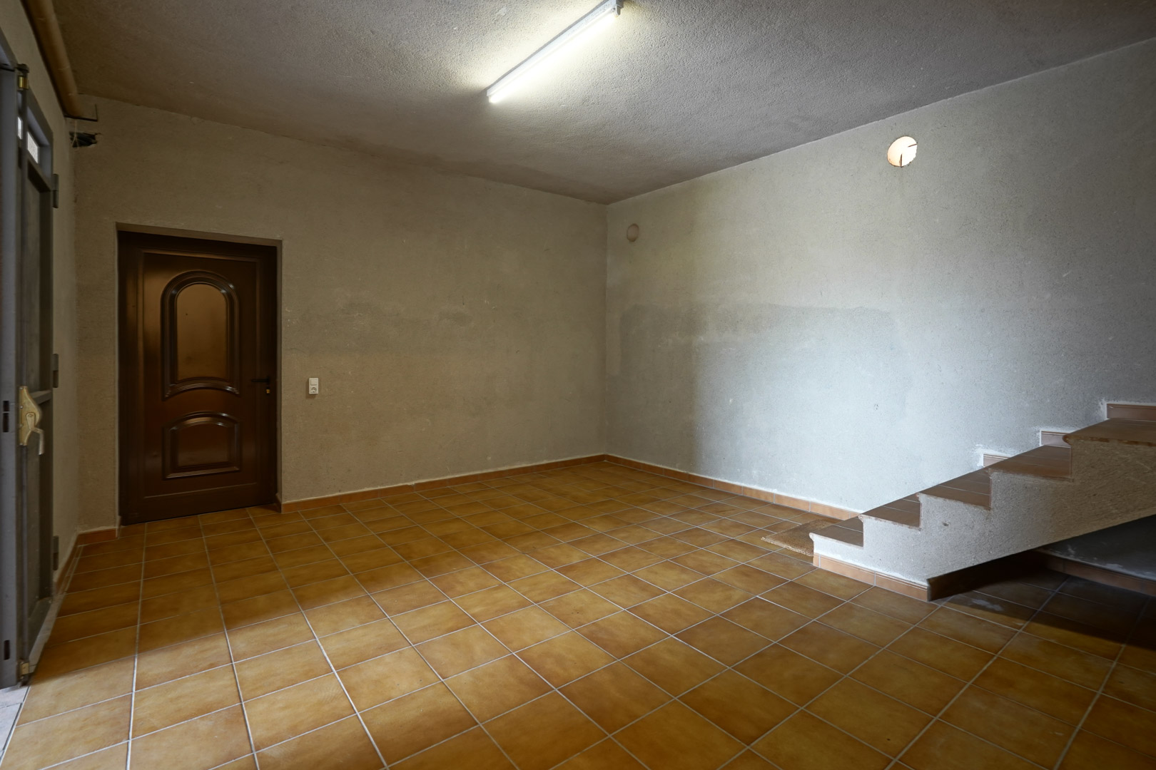 Functionele ruimte met terracotta vloertegels, ruw afgewerkte wanden en een betegelde trap naar de bovenverdieping.