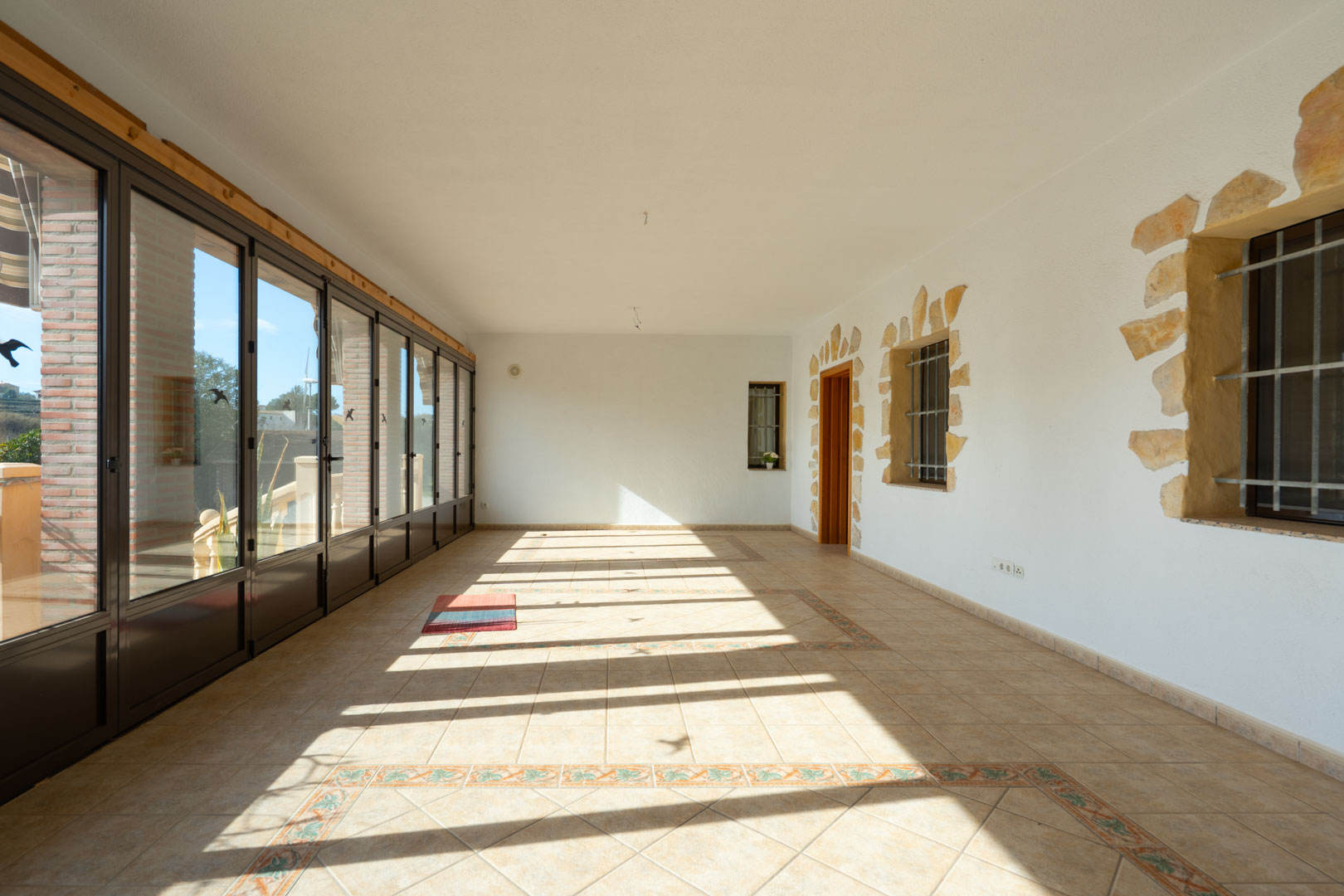 Ingebouwde veranda met grote glazen deuren, een decoratieve tegelvloer en witte muren met natuurstenen details rond de raamkozijnen.
