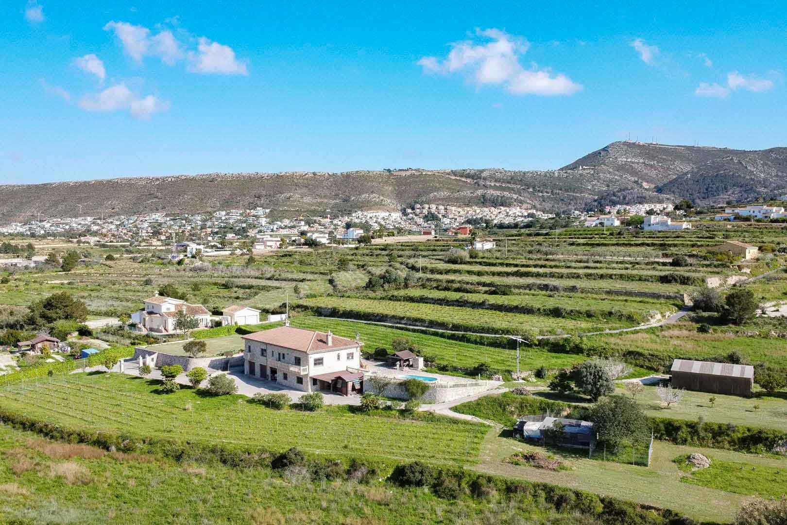 Luchtfoto van een stenen landhuis met twee verdiepingen, zwembad en terrasvormige landbouwgronden tegen een bergachtig decor.