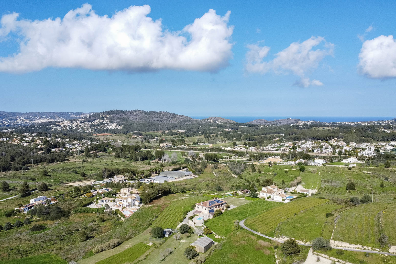 Panoramisch luchtaanzicht van het mediterrane landschap met groene valleien, verspreide villa's met zwembaden en uitzicht op de verre zee.