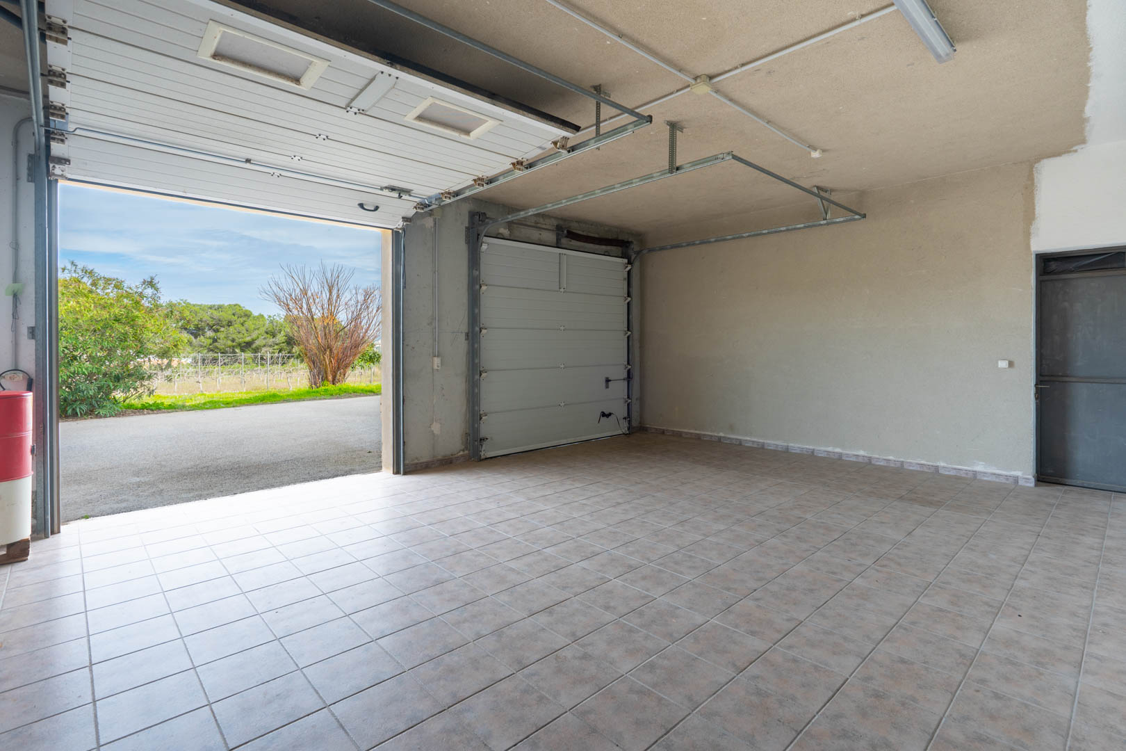 Ruime garage met keramische tegelvloer, voorzien van twee sectionaaldeuren en TL-verlichting. Biedt directe toegang tot de oprit en de omliggende tuin.