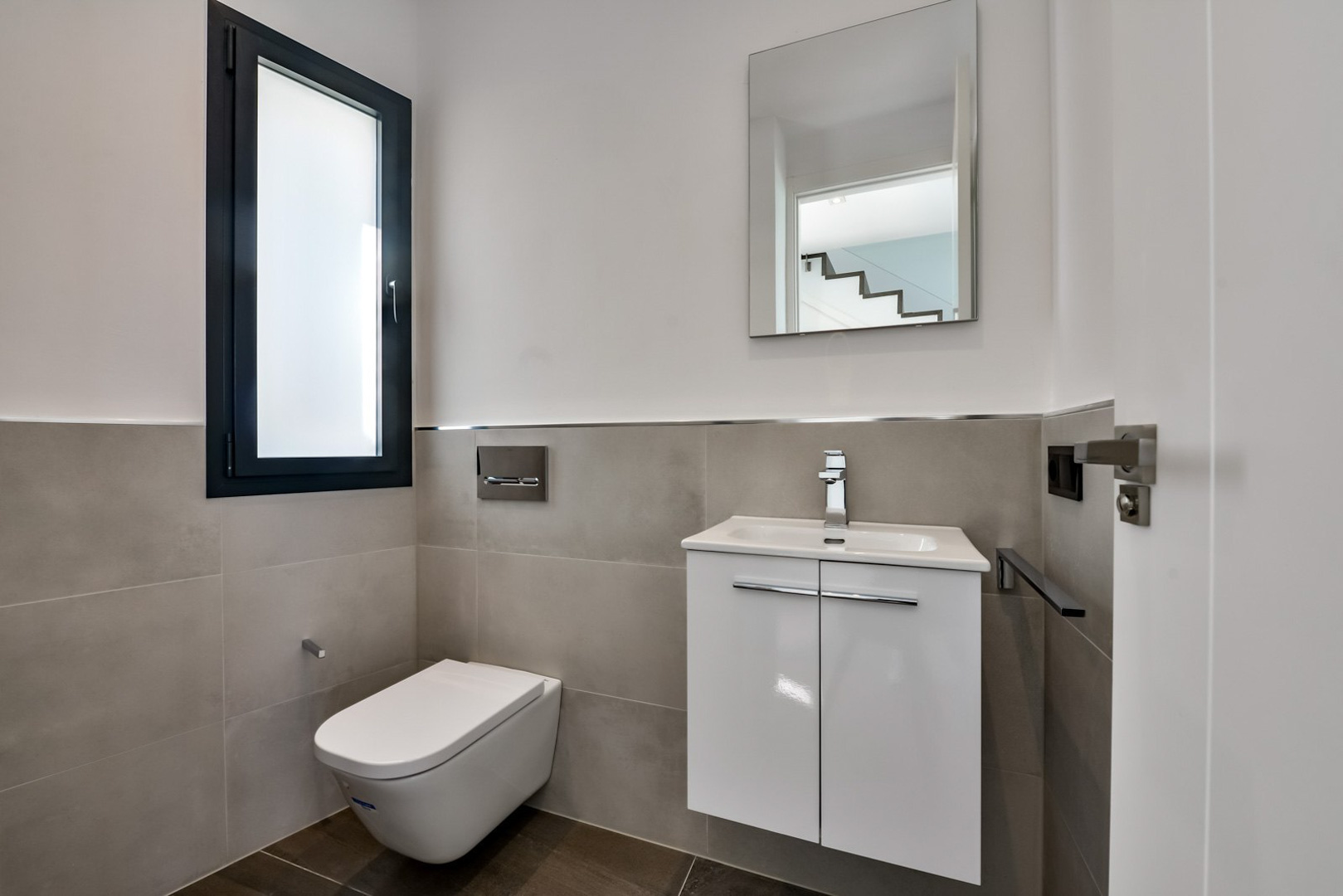 Gastentoilet met hangend toilet, minimalistisch wit wastafelmeubel en een raam van matglas met een donker kozijn.