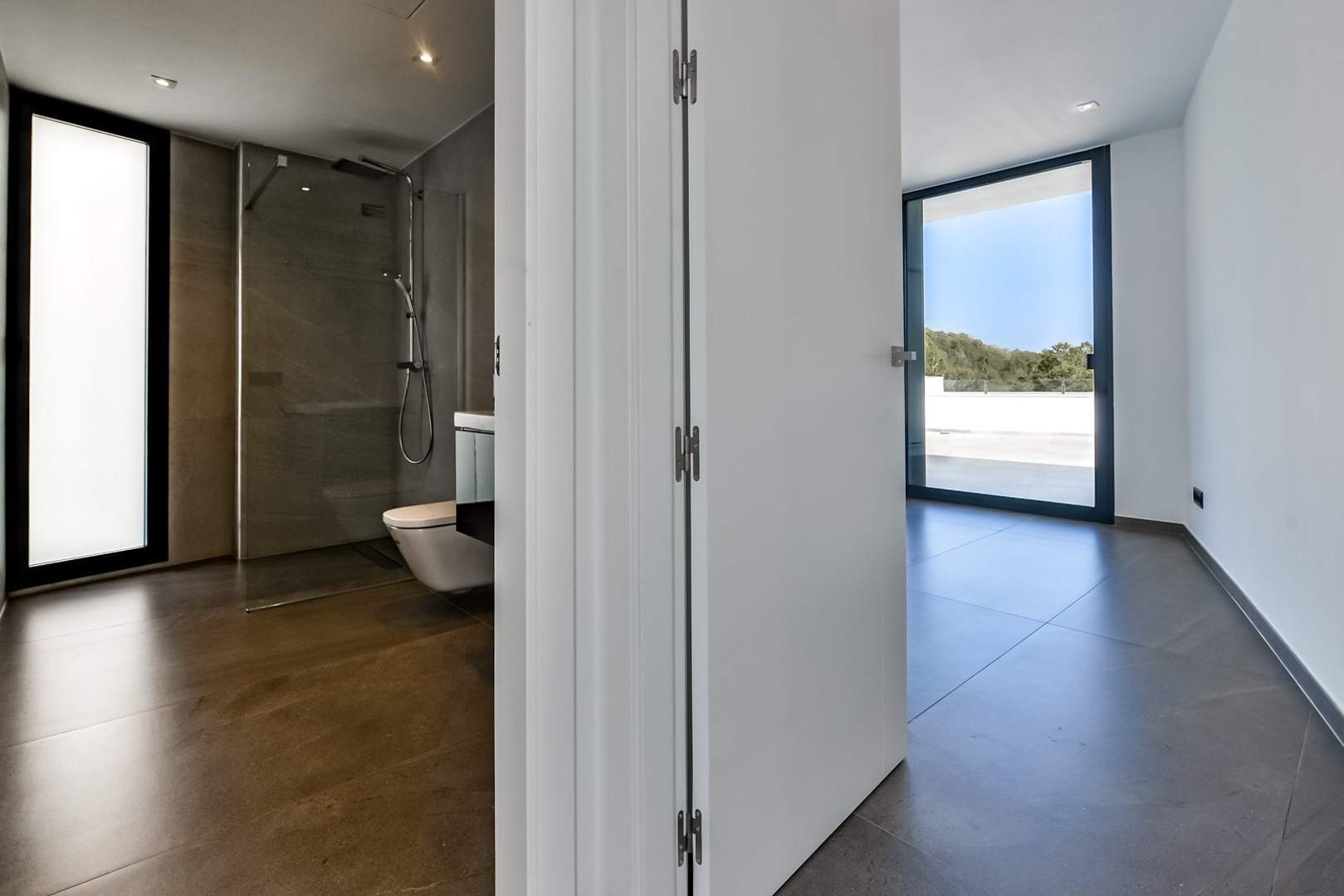 Hoofdslaapkamer met en-suite badkamer voorzien van inloopdouche, grootformaat tegels en directe toegang tot het terras via kamerhoge schuifdeuren.