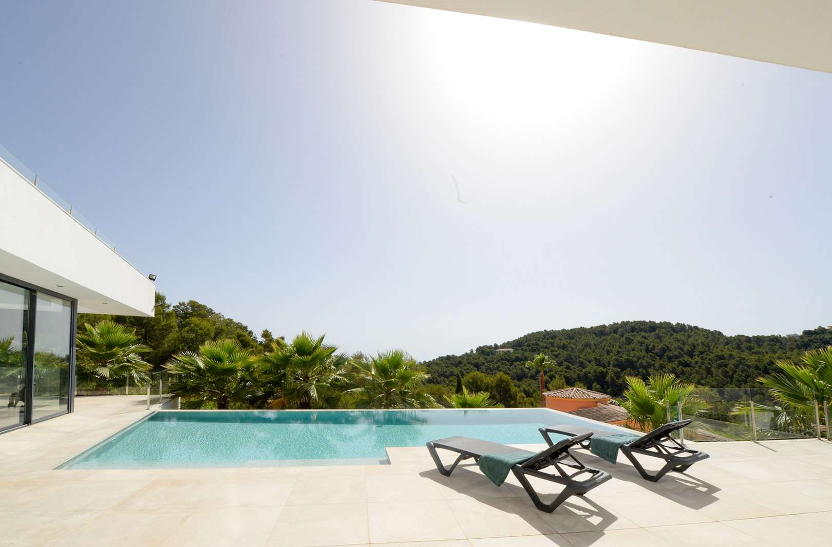 Infinity-zwembad en zonneterras met ligstoelen, met een weids uitzicht over de groene heuvels en de omliggende mediterrane vegetatie.