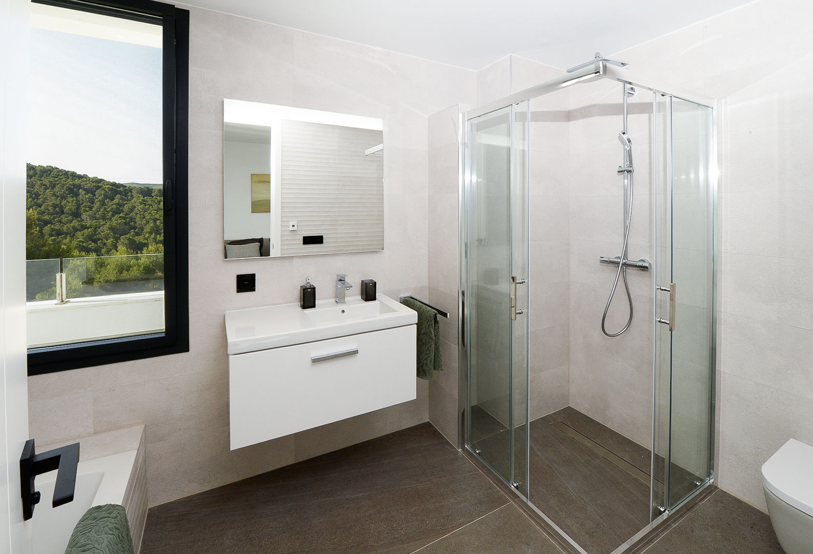 Moderne badkamer met glazen douchecabine, zwevend wit wastafelmeubel en een raam met uitzicht op de groene heuvels. Afgewerkt met neutrale tegels.