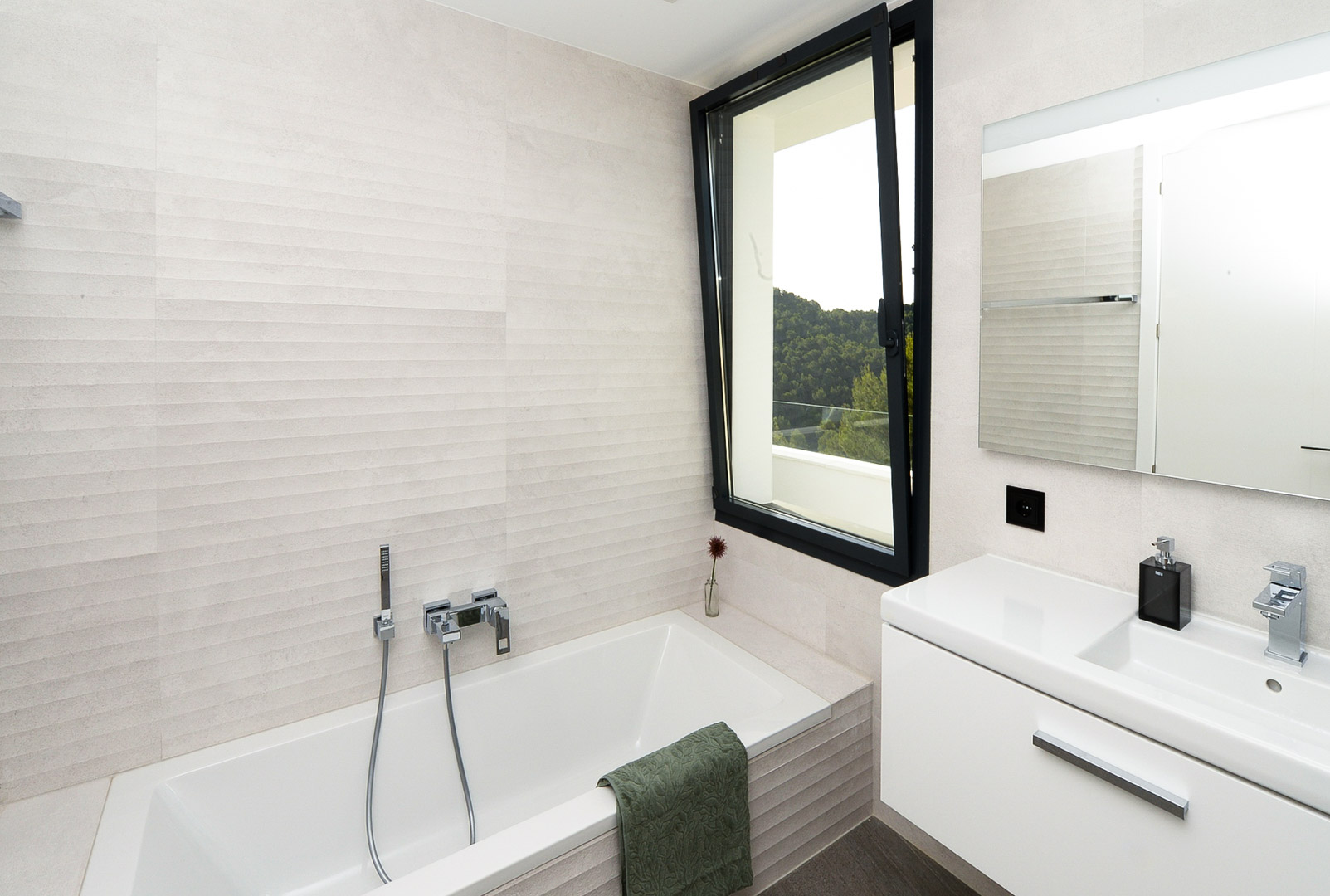 Moderne badkamer voorzien van een ingebouwd ligbad, getextureerde wandtegels en een raam met uitzicht op de groene heuvels.