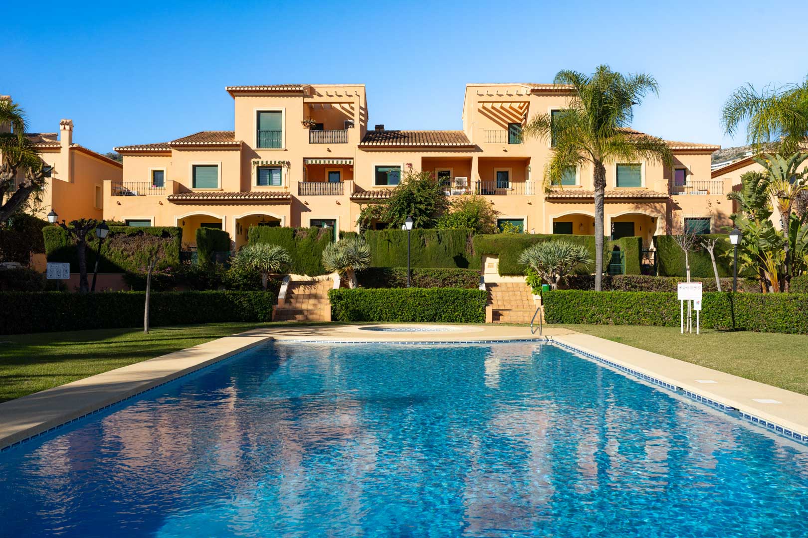 Gemeenschappelijk zwembad omgeven door mediterrane tuinen en gazons, met de traditionele architectuur van het Floridamar-complex op de achtergrond.
