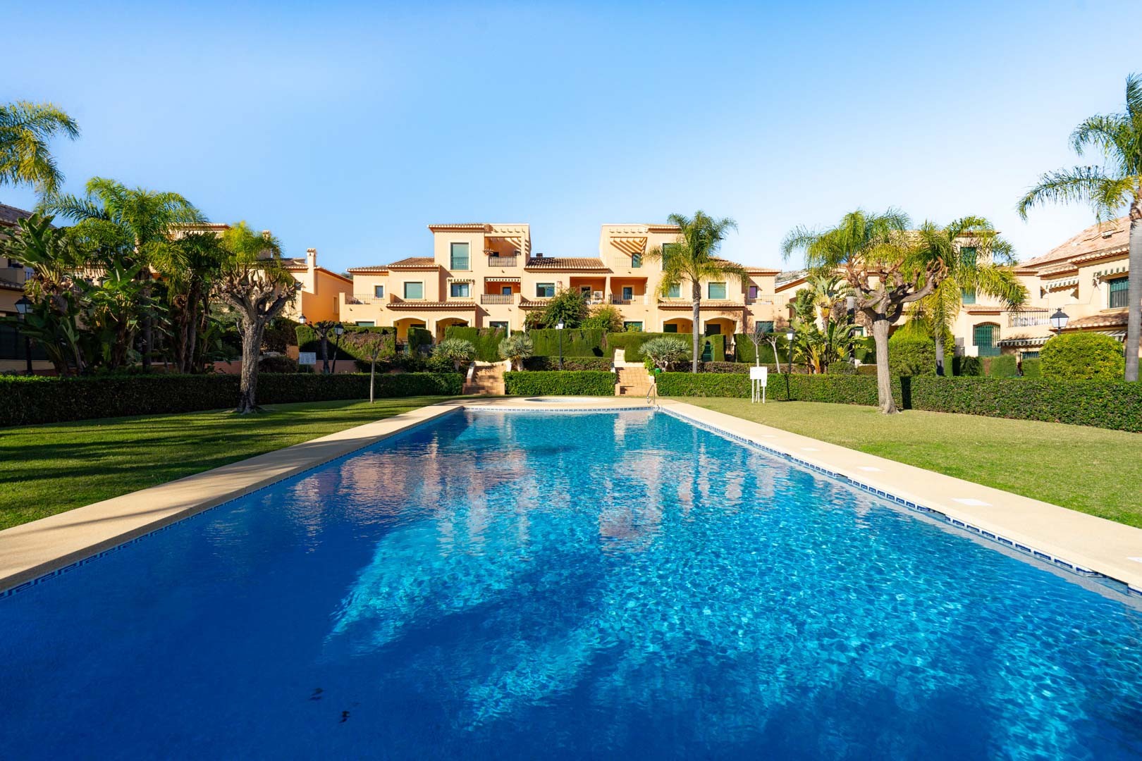Groot buitenzwembad omgeven door goed onderhouden gazons en mediterrane tuinen, met op de achtergrond de traditionele architectuur van het Floridamar-complex.