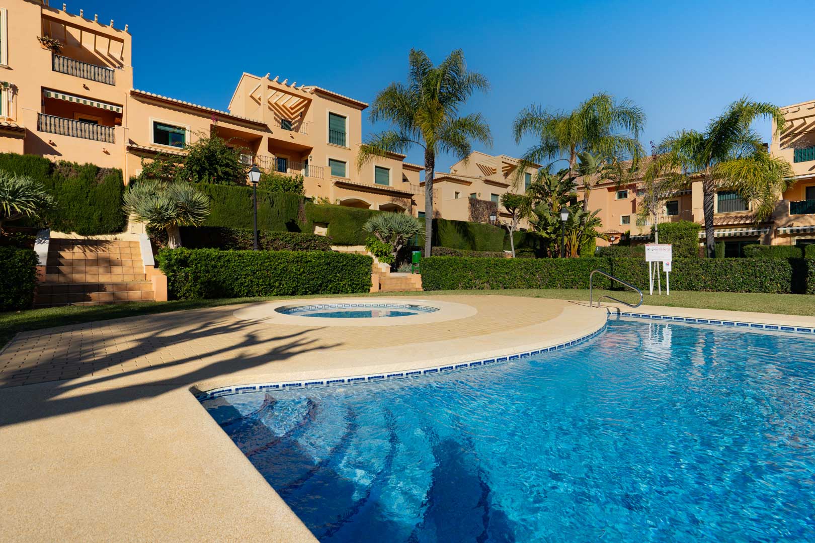 Groot gemeenschappelijk buitenzwembad met een rond kinderbad, omgeven door volgroeide tuinen, palmbomen en de mediterrane architectuur van Floridamar.