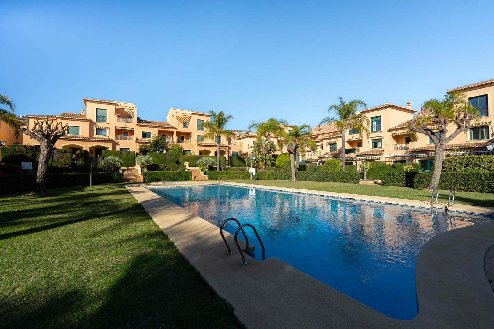 Groot gemeenschappelijk buitenzwembad omgeven door verzorgde gazons, palmbomen en mediterrane appartementengebouwen in het Floridamar-complex.