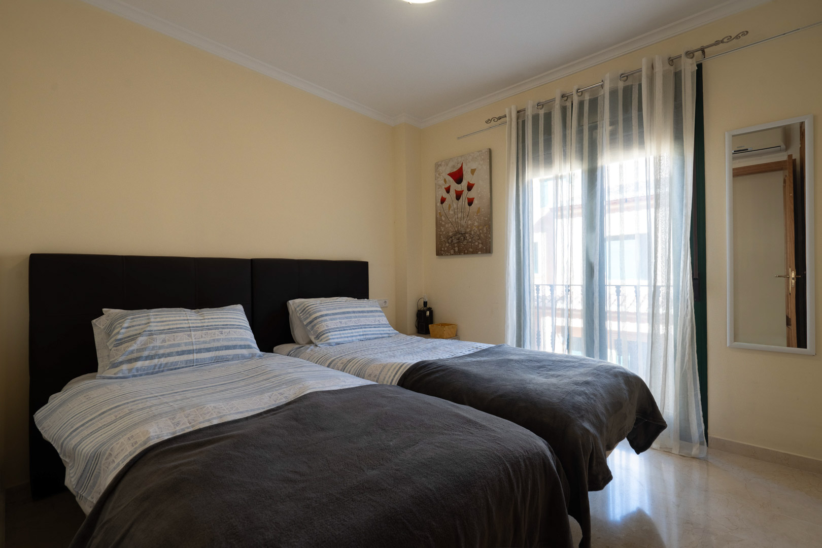 Lichte slaapkamer met twee eenpersoonsbedden, gepolijste marmeren vloer en directe toegang tot het balkon via grote ramen.