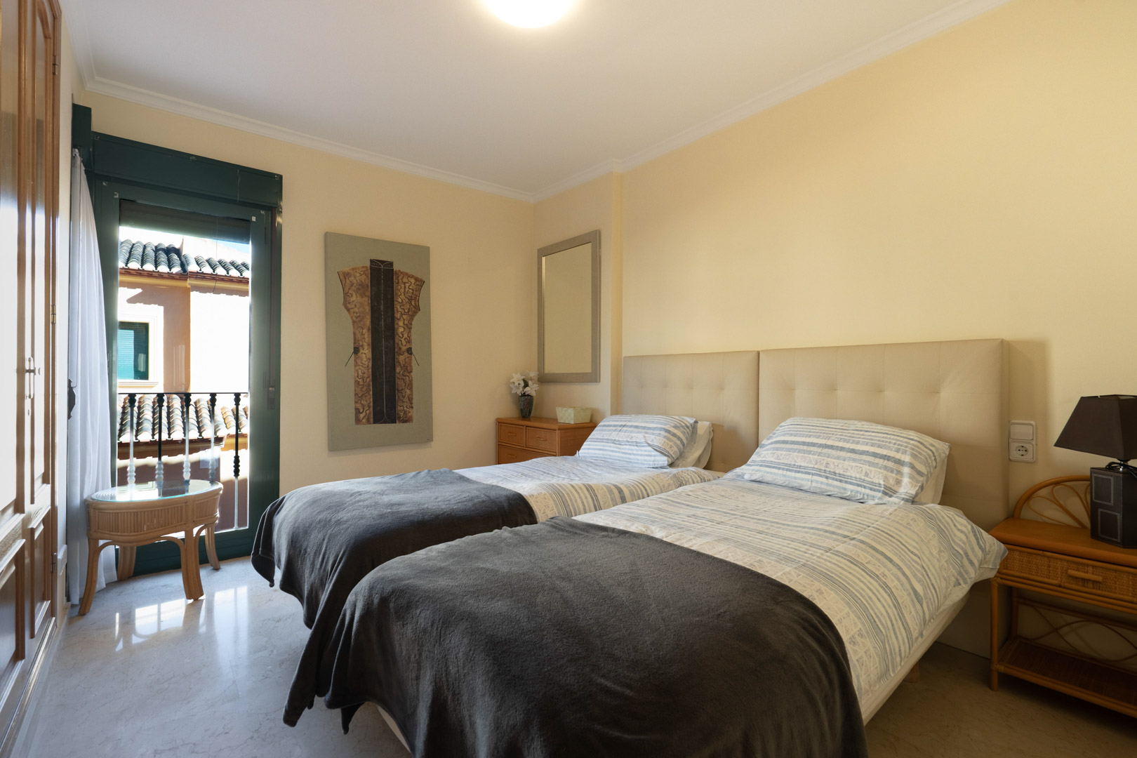 Lichte slaapkamer met twee eenpersoonsbedden, gevoerd hoofdbord, marmeren vloer en inbouwkasten. Directe toegang tot een privébalkon.