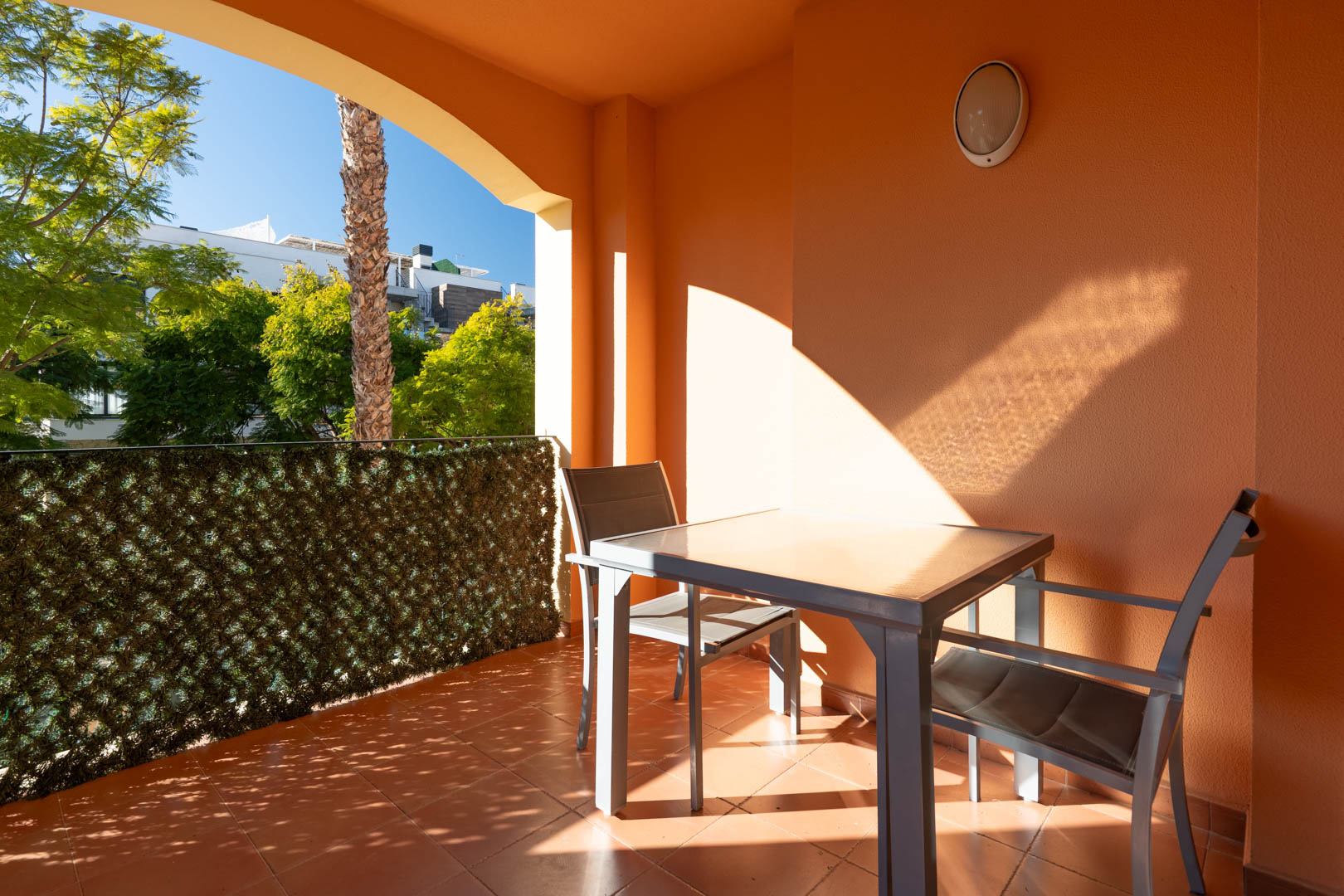 Overdekt terras met terracotta tegels, modern tuinmeubilair en uitzicht op de volgroeide tuinen van het complex.