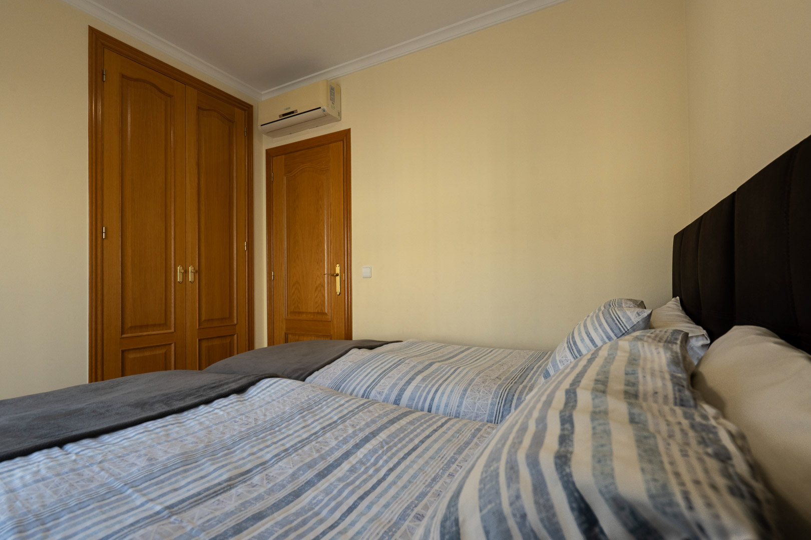 Slaapkamer met klassieke ingebouwde houten kasten, split-airconditioning en bedden voorzien van een donker gestoffeerd hoofdbord.