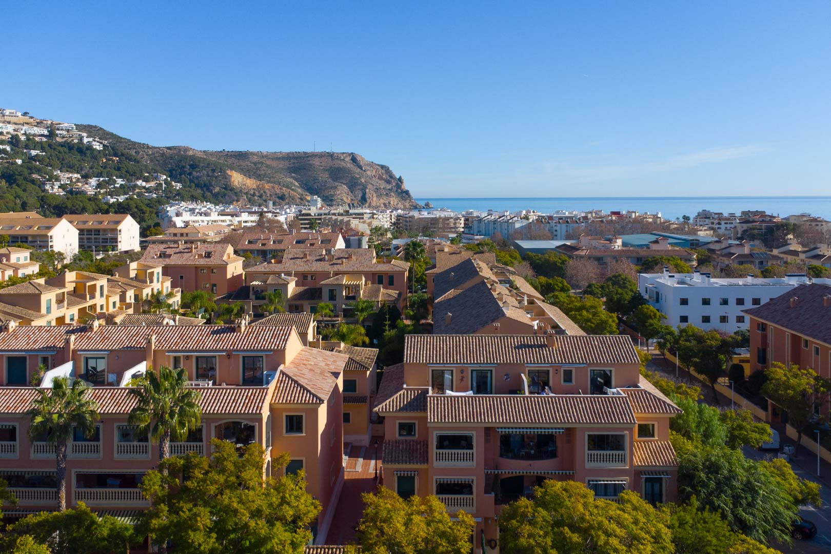 Verhoogd panoramisch uitzicht op het Floridamar-complex met terracotta daken, uitzicht op de Middellandse Zee en de Cabo de San Antonio op de achtergrond.