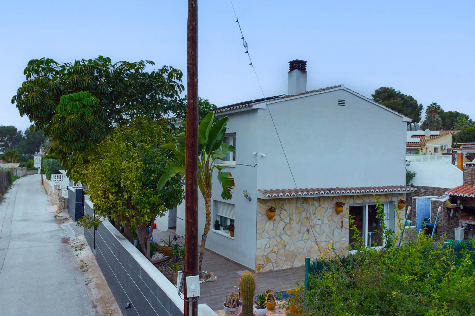 Exterieur van de villa met witte gevel en natuurstenen bekleding, omgeven door mediterrane beplanting en voorzien van zonnepanelen op het dak.