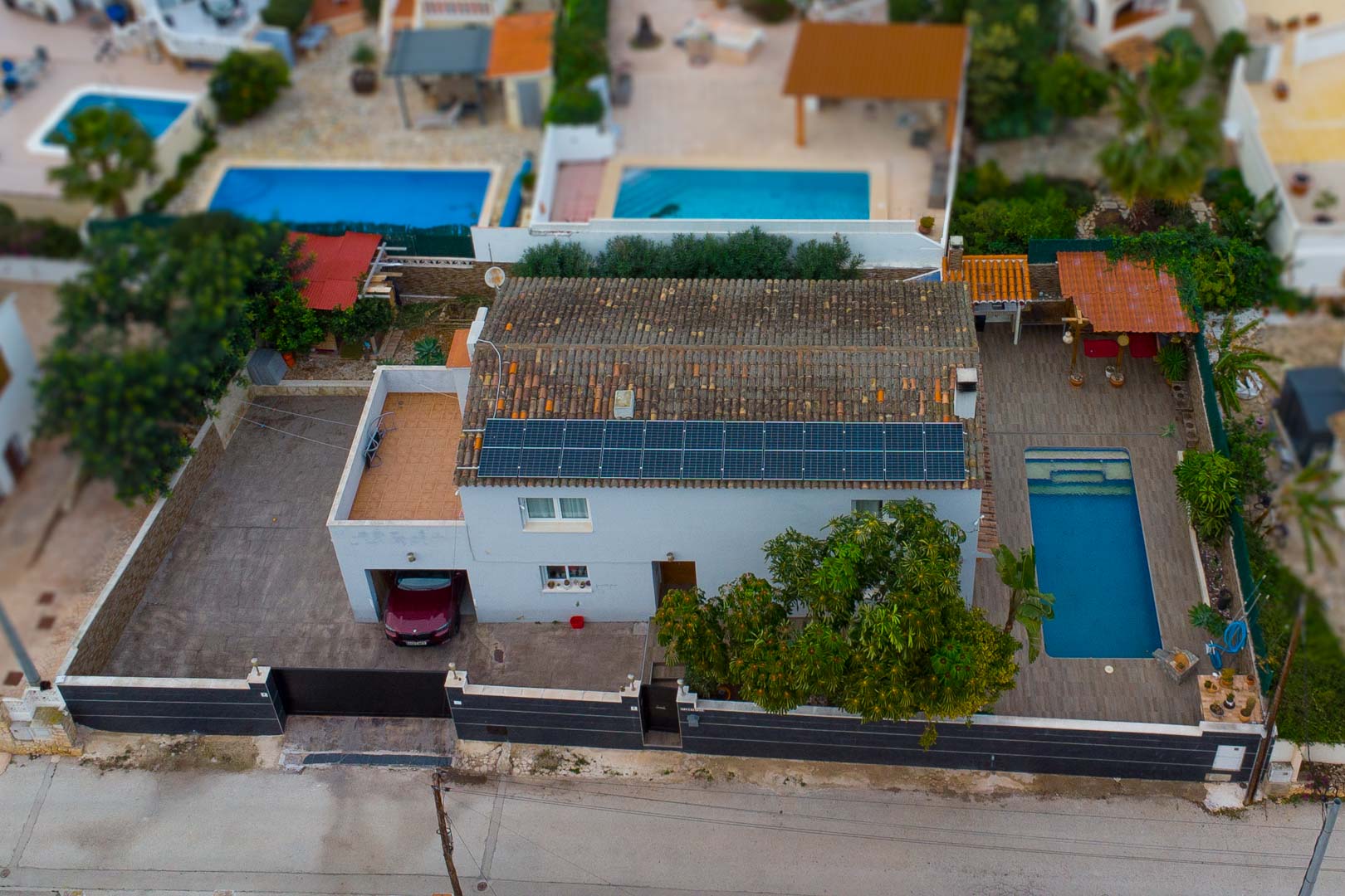 Luchtfoto van de villa met zonnepanelen op het dak, een privézwembad met terras en een inpandige garage op een volledig omheind perceel.