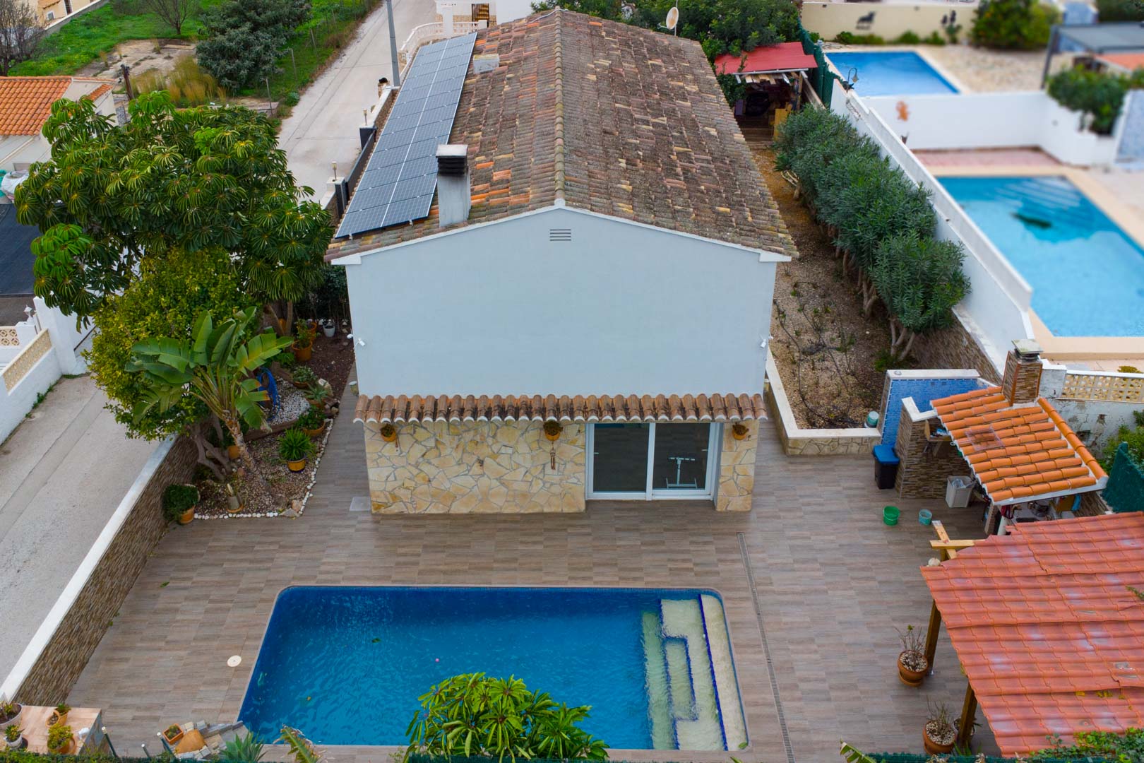 Luchtfoto van de villa met zonnepanelen op het dak, privézwembad en een betegeld terras met overdekte buitenkeuken.