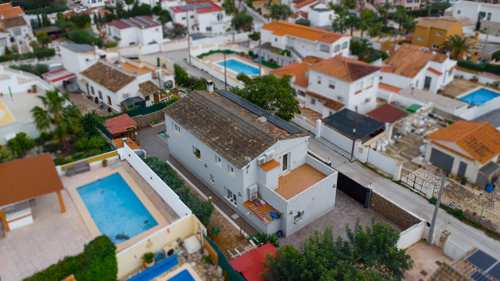 Luchtfoto van de villa met zonnepanelen op het pannendak, een terras op de bovenverdieping en de ligging in een rustige woonwijk in Calpe.
