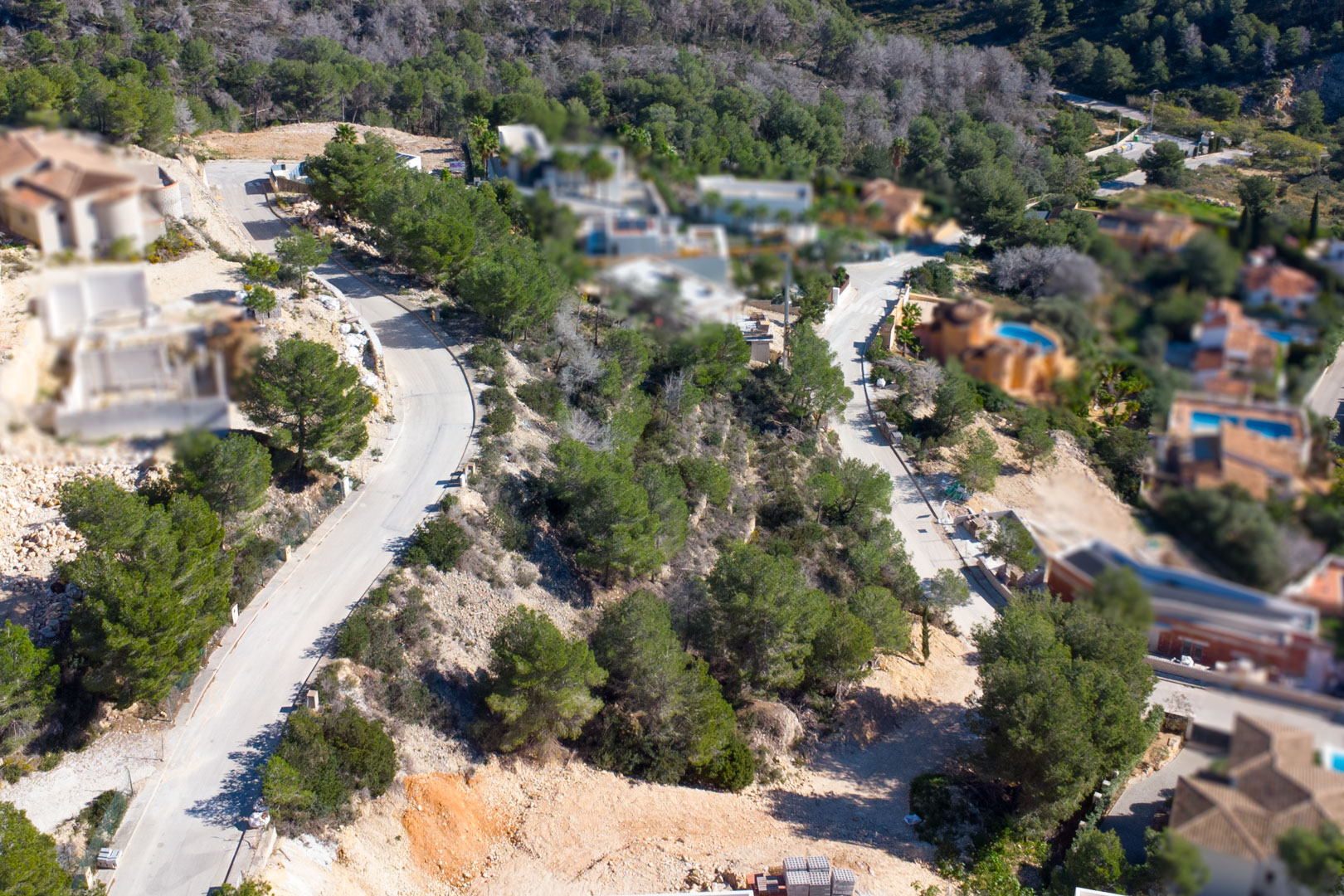 Luchtfoto van de urbanisatie Tosalet 5 in Jávea, met geasfalteerde wegen, bouwpercelen op hellingen omgeven door pijnbomen en omliggende villa's.