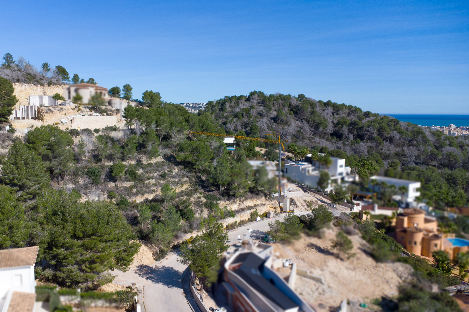Verhoogd overzicht van de urbanisatie Tosalet 5 in Jávea, met bouwpercelen op een helling omgeven door pijnbomen en uitzicht op de Middellandse Zee.