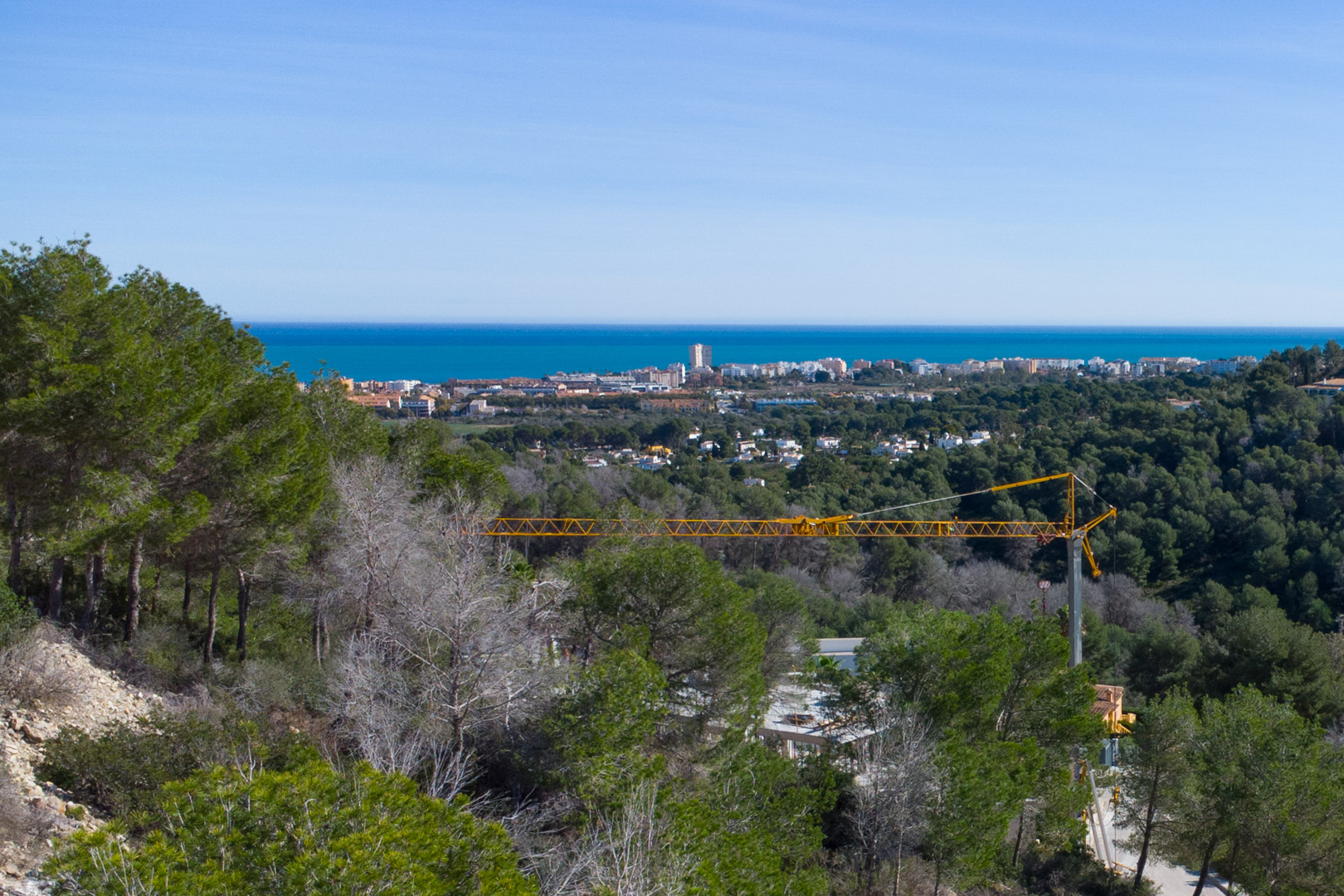 Verhoogd panoramisch uitzicht op de Middellandse Zee en de kustlijn van Jávea, omgeven door pijnbomen met een heldere blauwe horizon.