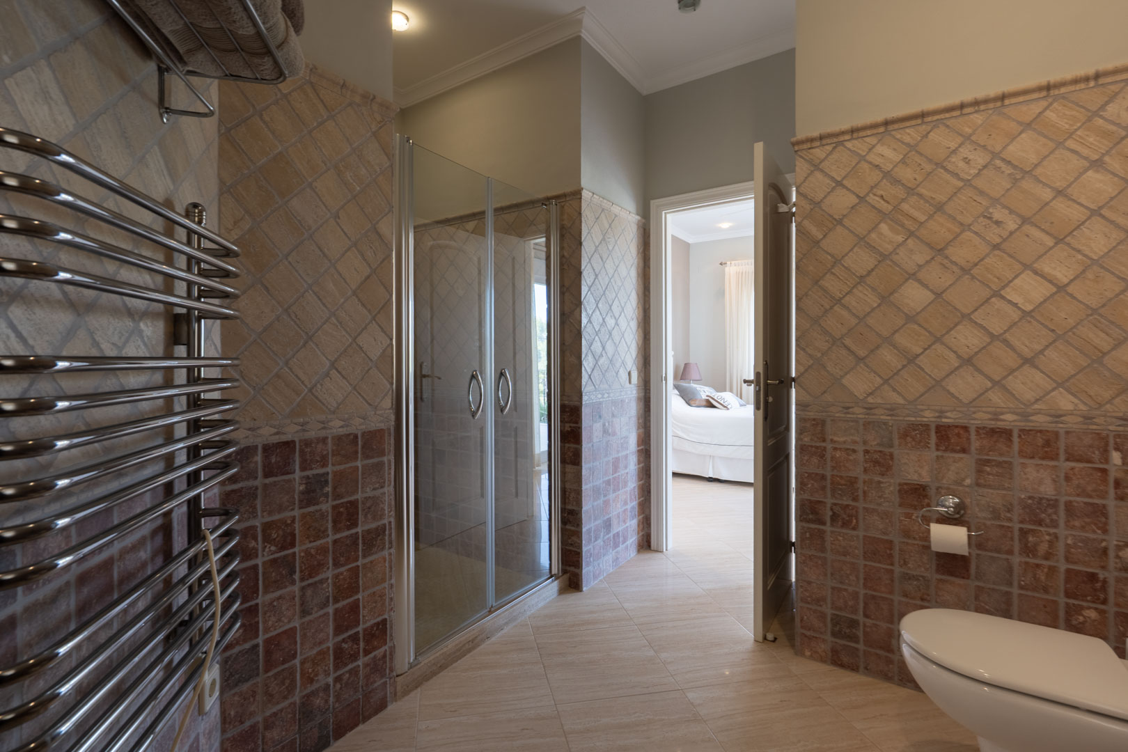 En-suite badkamer met glazen douchecabine, chromen handdoekradiator en tweekleurige wandbetegeling, direct verbonden met de slaapkamer.
