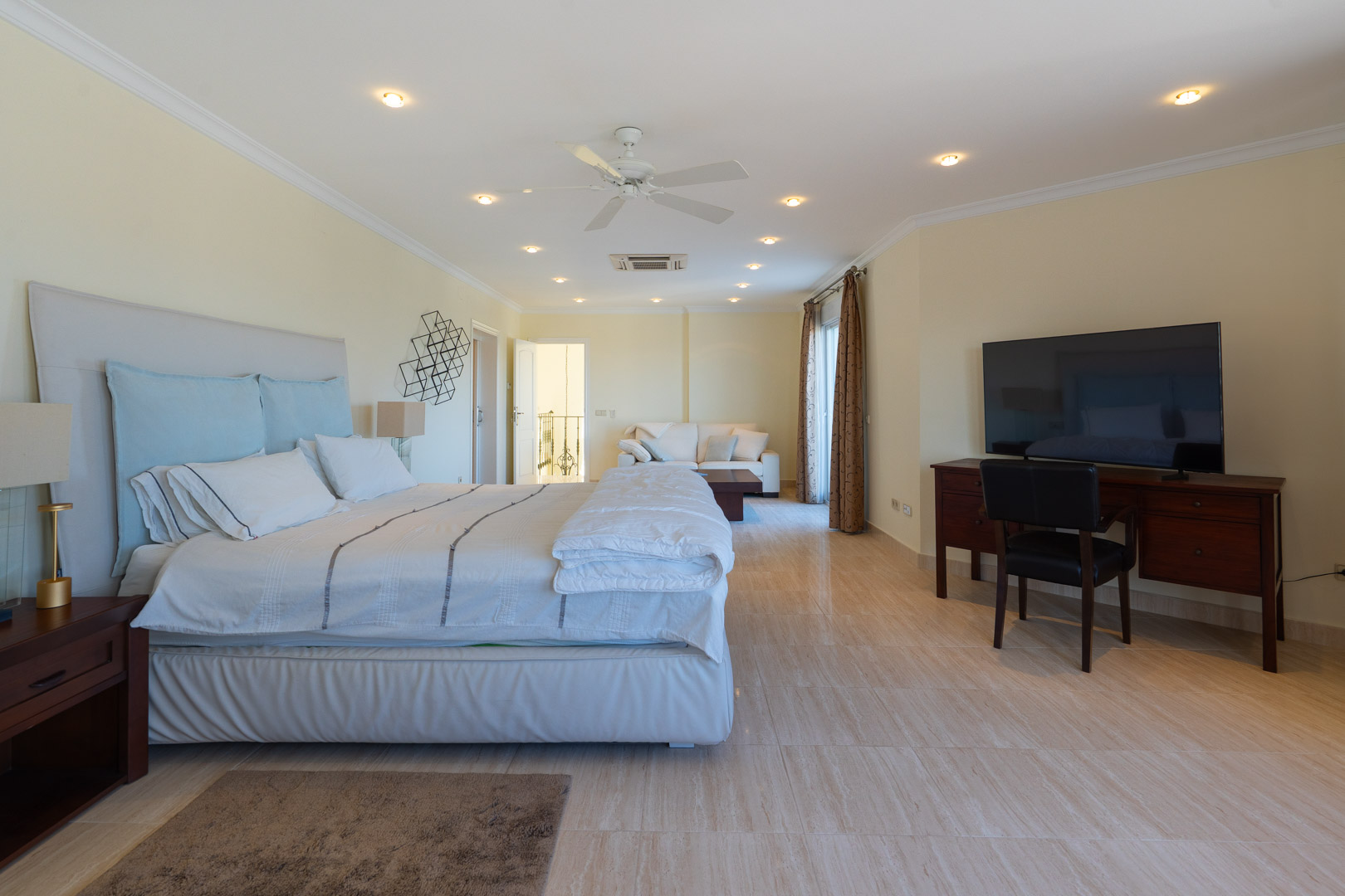 Master suite met gepolijste stenen vloeren, een geïntegreerde zithoek met bank, een houten bureau en inbouwspots in het plafond.