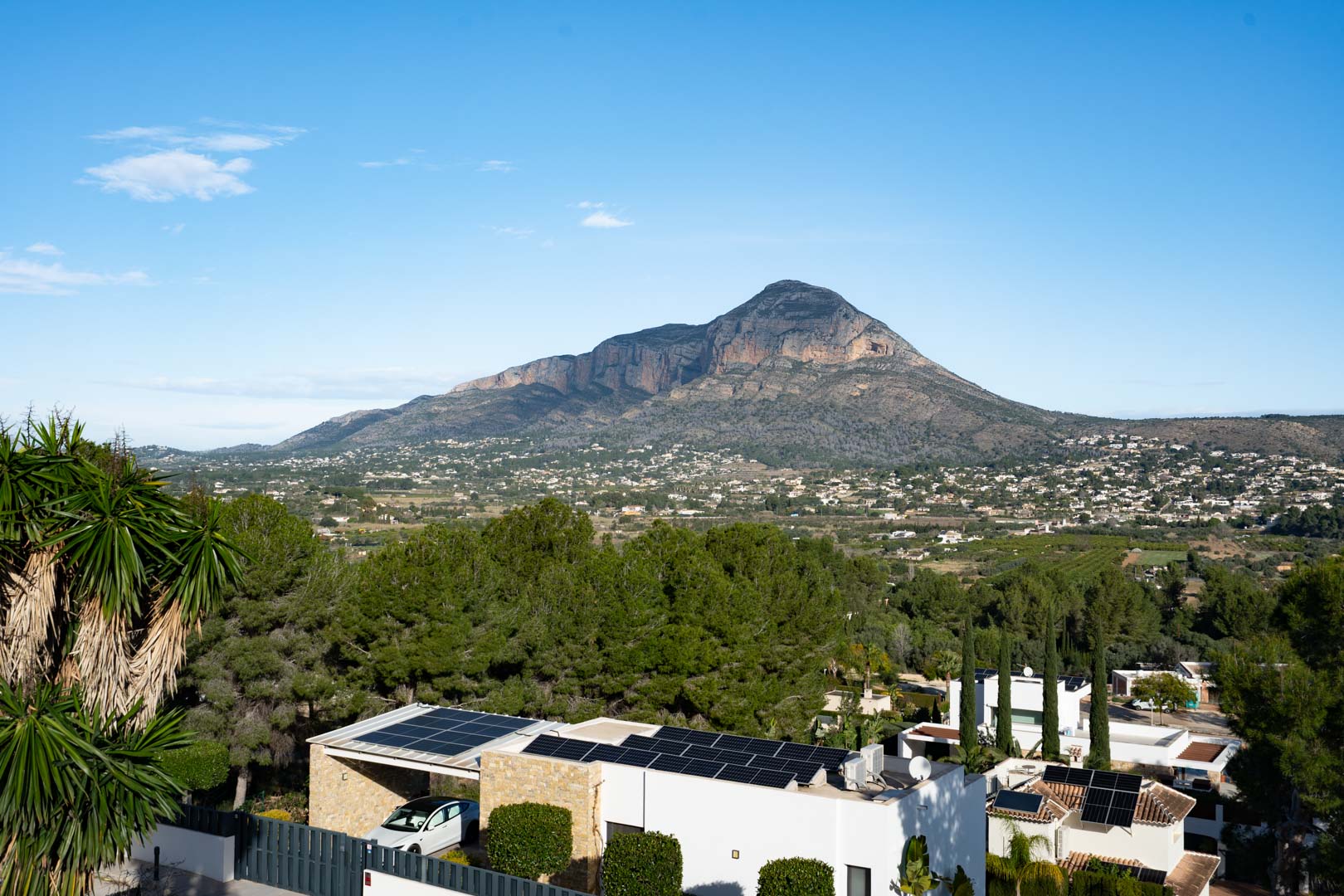 Panoramisch uitzicht op de Montgó-berg vanaf het perceel, met zicht op de zonnepanelen op het dak en de residentiële omgeving te midden van pijnbomen.