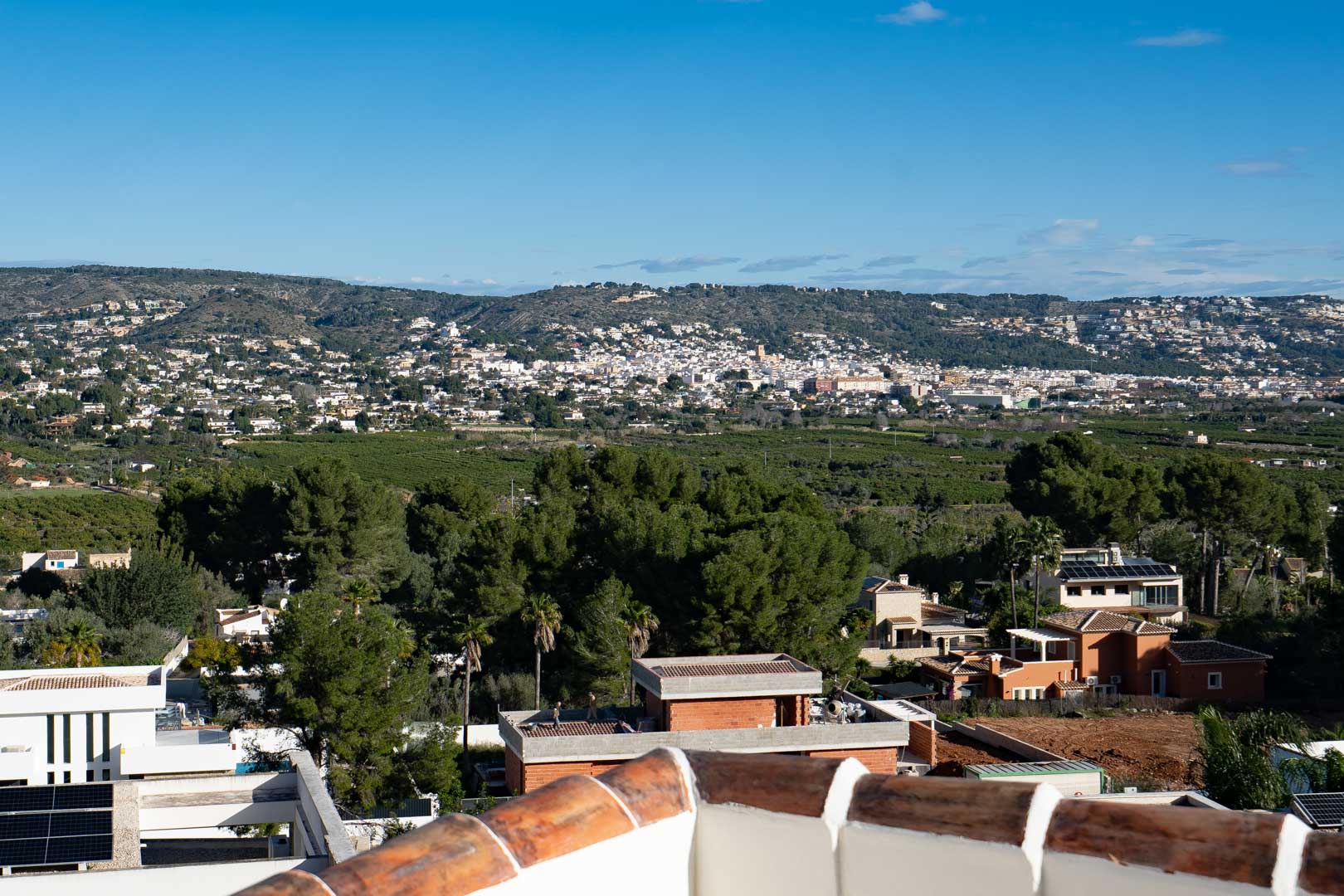 Panoramisch uitzicht vanaf het boventerras over de vallei en de heuvels, met een blik op de mediterrane vegetatie en de omliggende woonwijk.