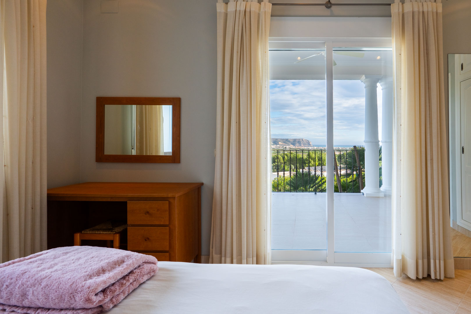 Slaapkamer met houten bureau en directe toegang tot een privéterras met witte zuilen en panoramisch uitzicht op zee en de Montgó.