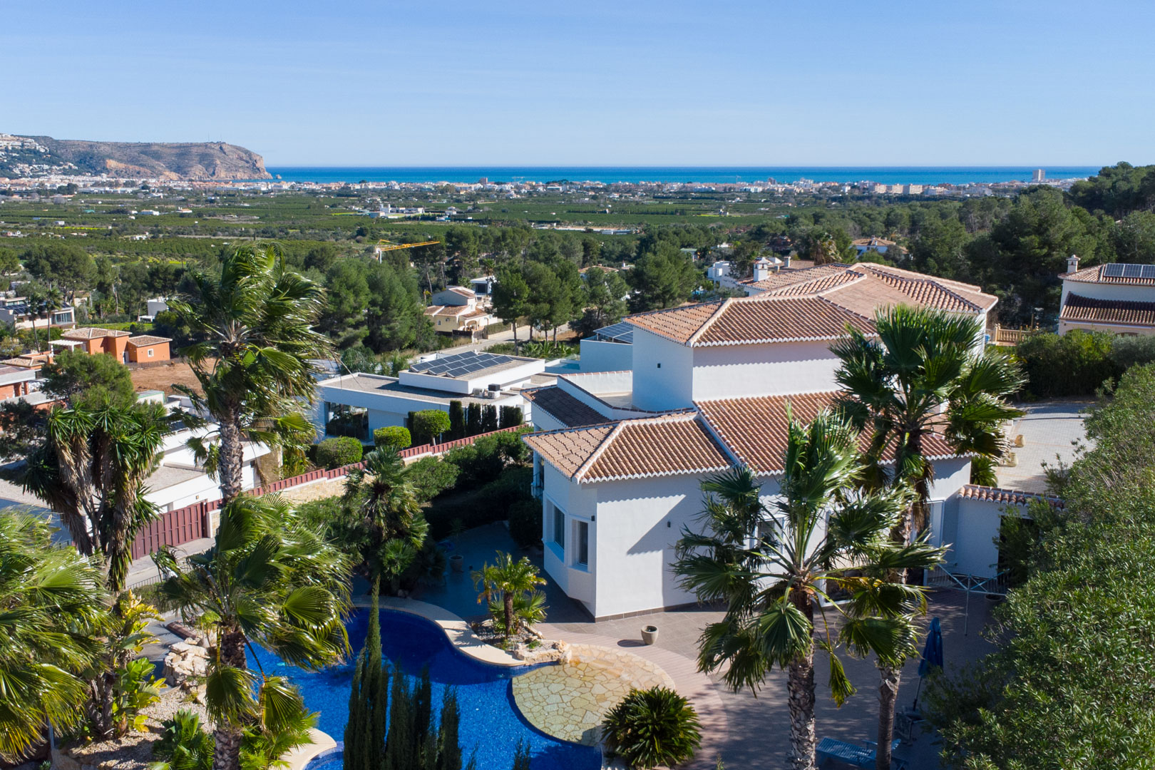 Verhoogd aanzicht van de witte villa met zwembad, volgroeide palmbomen en een panoramisch uitzicht over de Middellandse Zee.