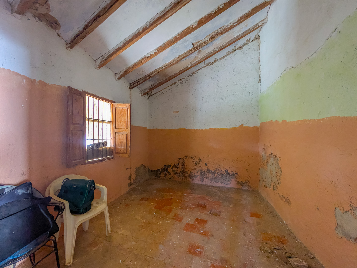 Binnenruimte met een schuin plafond met houten balken, een traditionele terracotta tegelvloer en een raam met originele houten luiken.