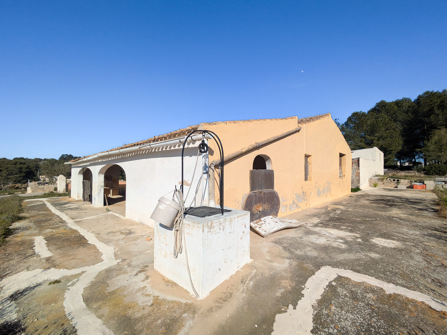 Exterieur van de traditionele finca met een boogvormige veranda, een authentieke waterput en een ruim stenen terras in de volle zon.