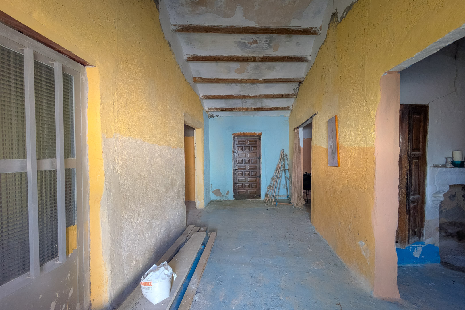 Interne gang met hoge plafonds met houten balken en rustieke muren, die het authentieke karakter en het renovatiepotentieel van de woning tonen.