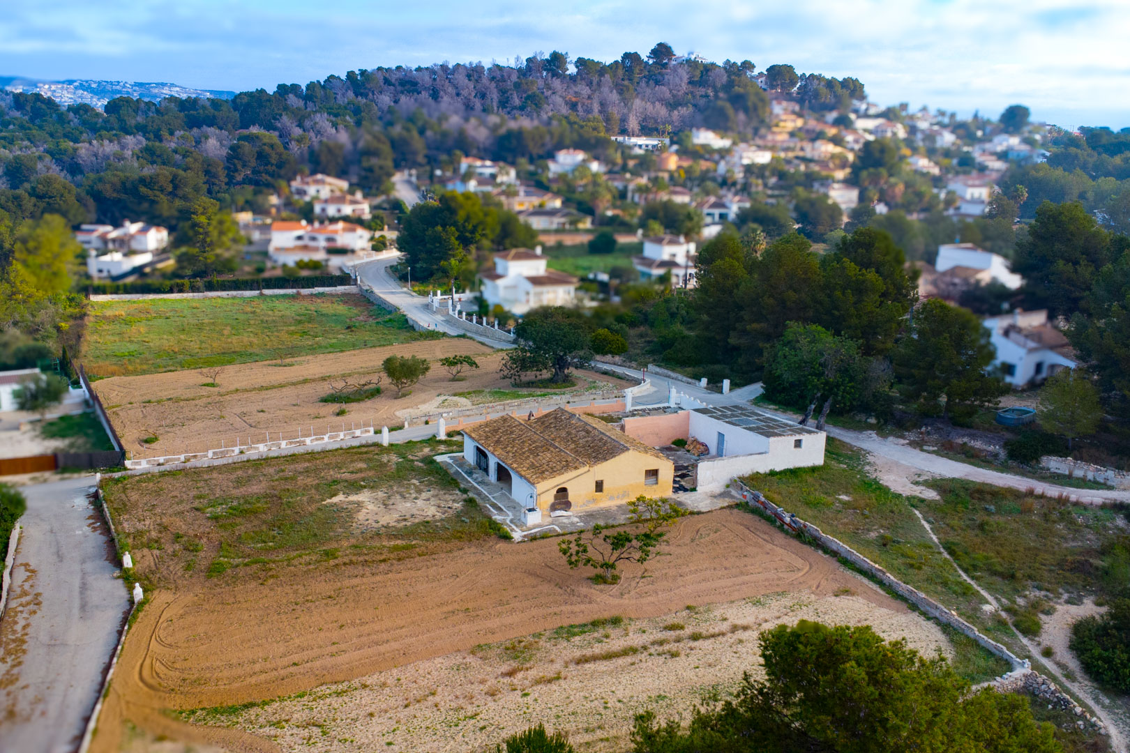 Luchtfoto van de traditionele finca met pannendak en okergele gevel, gelegen op een groot rustiek perceel omgeven door groen en residentiële villa's.