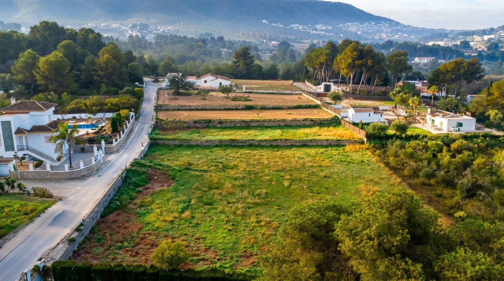 Luchtfoto van het rustieke perceel met traditionele stenen terrassen, omgeven door dennenbossen en met de bergen van Jávea op de achtergrond.