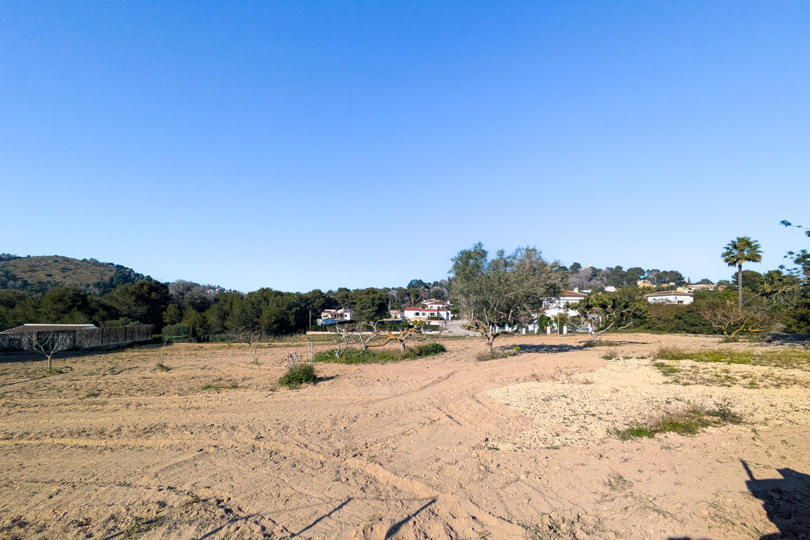 Panoramisch uitzicht op het uitgestrekte, vlakke rustieke perceel met omgeploegde aarde, verspreide bomen en uitzicht op de omliggende heuvels van Jávea.