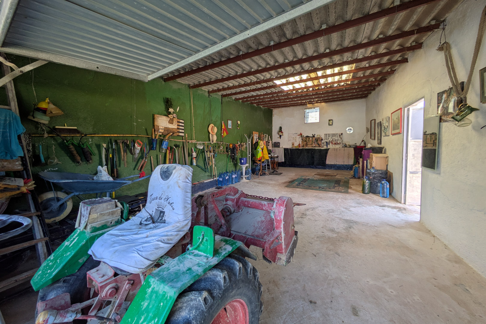 Ruime werkplaats of opslagruimte met betonvloer en hoge plafonds met metalen balken, geschikt voor landbouwmachines en gereedschap.