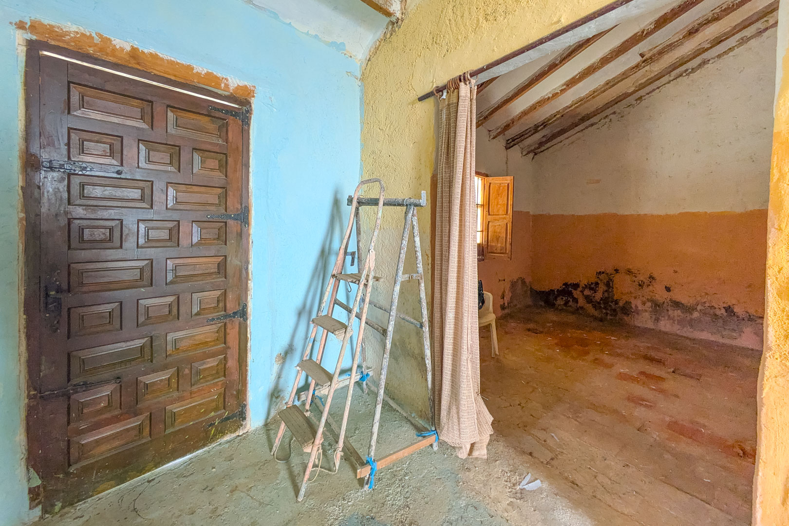 Rustiek interieur met een traditionele houten paneeldeur, gekleurde muren en originele balkenplafonds, ideaal voor een volledig renovatieproject.
