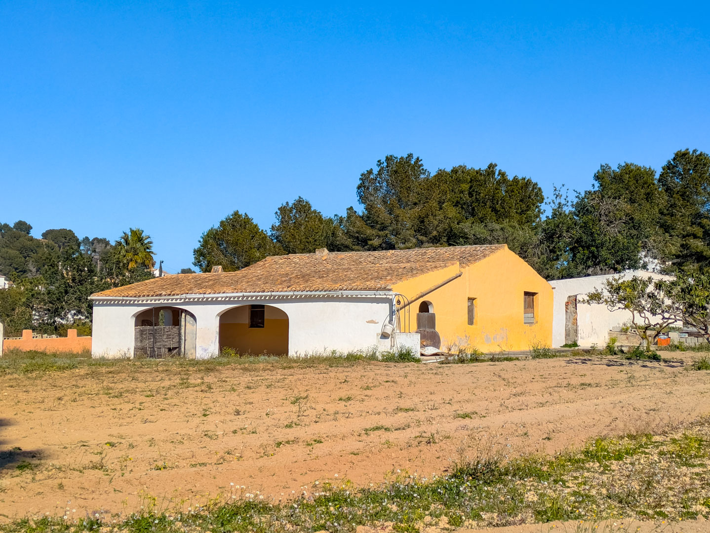 Traditionele finca met karakteristieke bogen en een pannendak, gelegen op een groot rustiek perceel omgeven door mediterrane pijnbomen.
