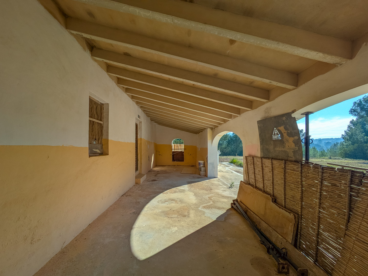 Traditionele overdekte veranda met houten balkenplafond en okerkleurige muren, uitkijkend over het natuurlijke landschap van Jávea.