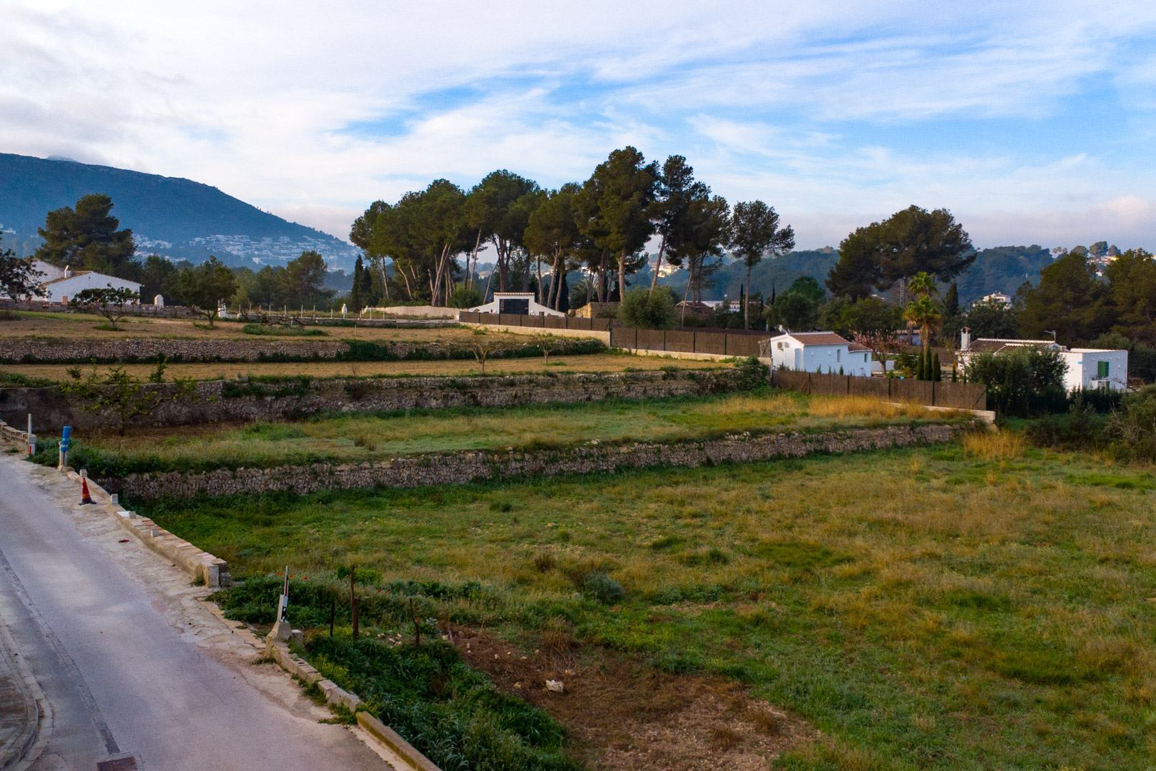 Uitzicht op de drooggestapelde stenen terrassen op het ruime rustieke perceel, omgeven door mediterrane vegetatie en bergzicht.