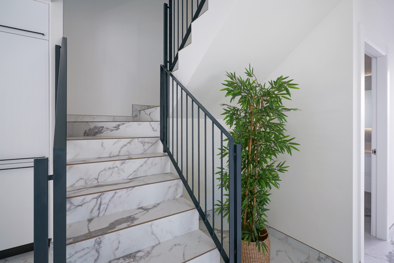 Binnentrap met treden van porselein met marmereffect en een minimalistische zwarte metalen leuning, die de verdiepingen in een modern design verbindt.