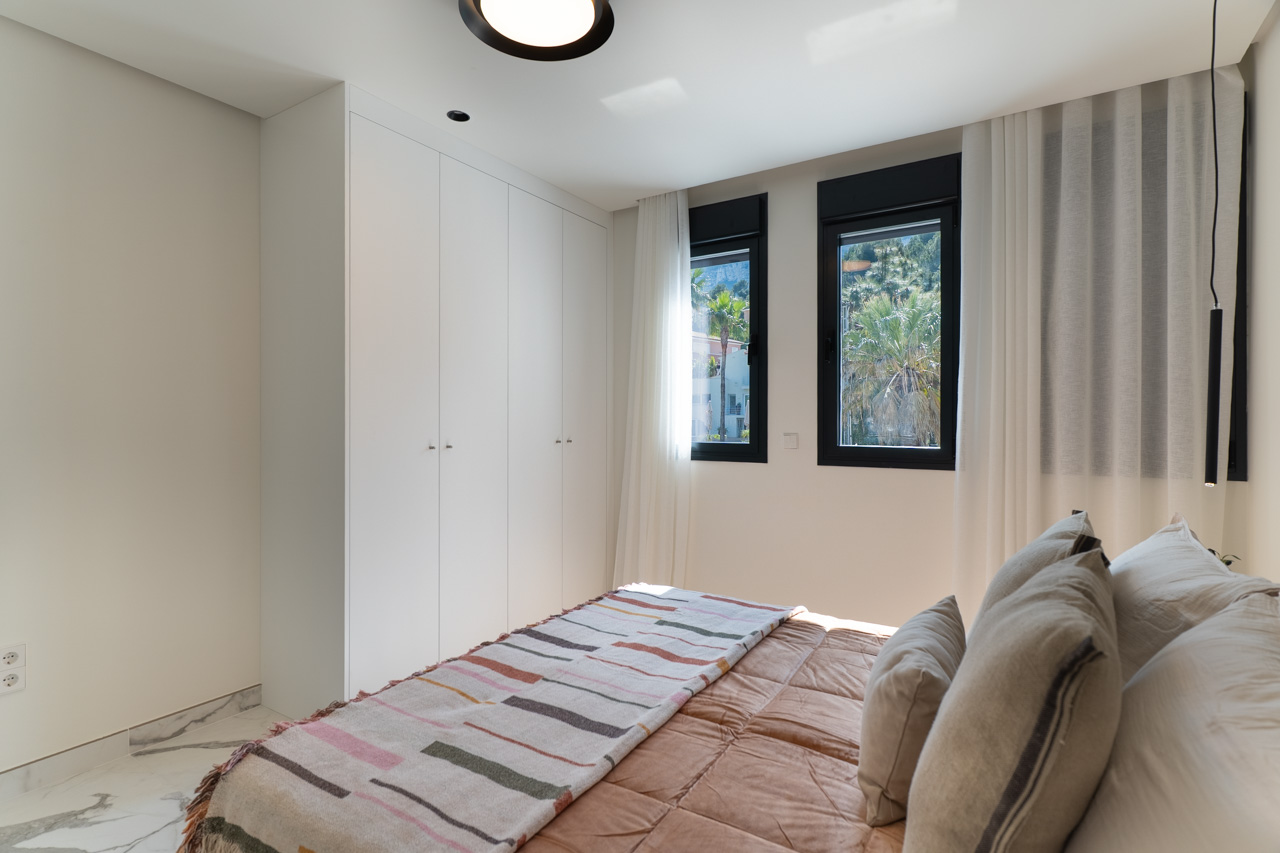 Lichte slaapkamer met kamerhoge witte inbouwkasten, marmeren vloer en ramen met uitzicht op het omliggende groen.