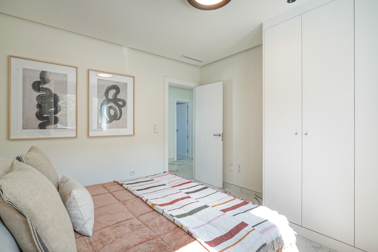 Lichte slaapkamer met kamerhoge witte inbouwkasten, porseleinen vloer met marmereffect en minimalistische wanddecoratie met abstracte kunst.